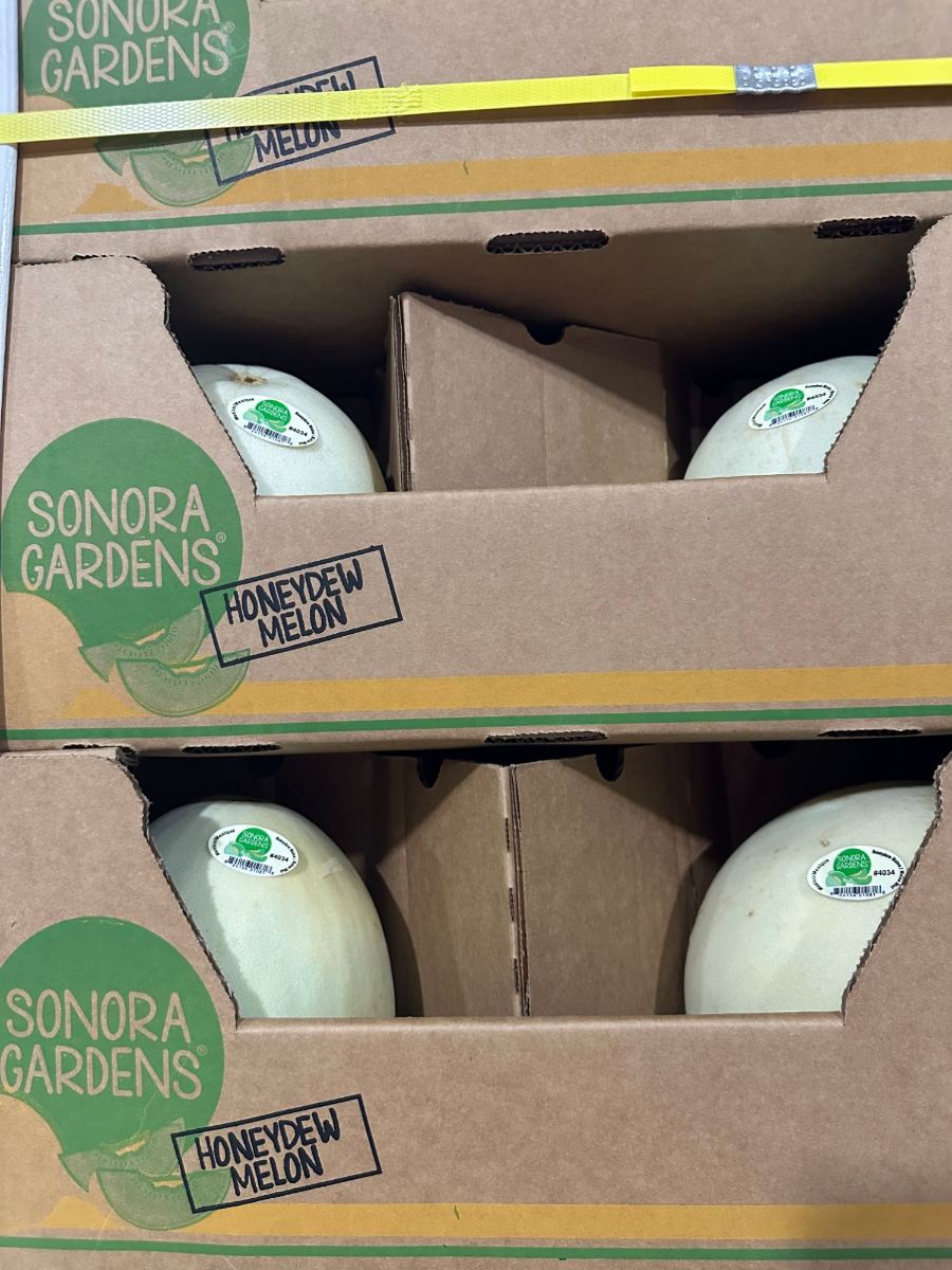 Cajas Sonora Gardens de melón honeydew apiladas en una tarima flejada, cada melón con una etiqueta Sonora Gardens